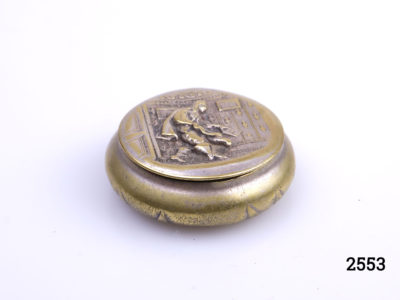 Antique brass pill or snuff box. Scene of cloaked man holding a sealed letter to the lid (Possibly a Royal messenger). Foliage pattern on the reverse (base) Measures 38mm in diameter at base. Photo of box from a lower angle showing depth