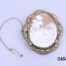 Vintage large pinchbeck cameo brooch. Intricately carved cameo of a man and woman holding hands and seated outdoors by a pond. Incredible detailing in the cameo carving. of an unusual scene. Main photo of brooch displayed on a flat surface with safety chain and pin laid out to the left