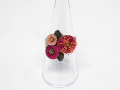 Pink flowers costume jewellery ring. Sweet white metal adjustable ring with a trio of different pink coloured felt flowers. Made in France by Taratata. Unadjusted size P / 7.5 Ring front measures approximately 20mm by 15mm.  Main photo of ring on a clear display stand and seen from the front