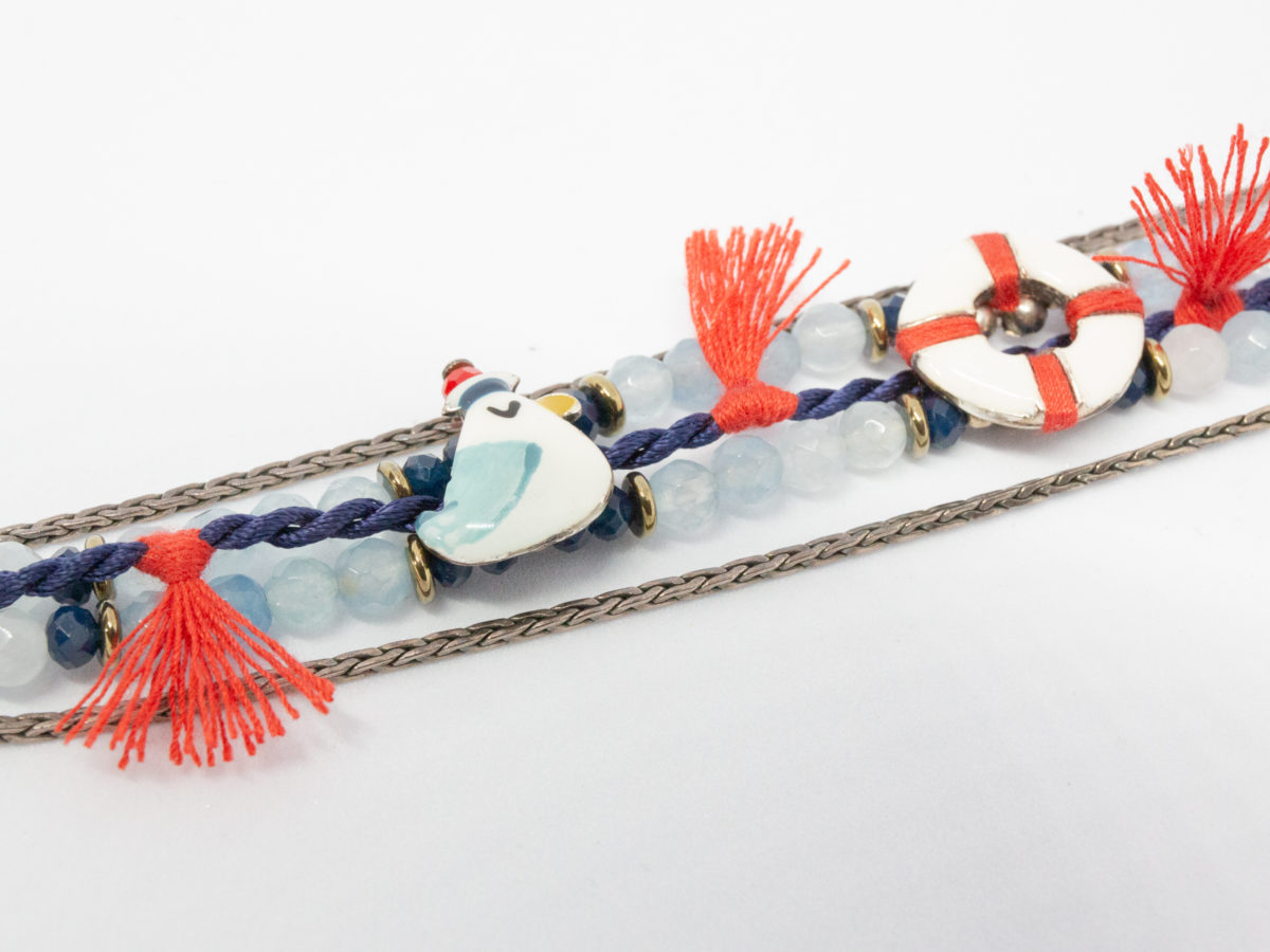 Costume jewellery bracelet with seagulls. Lovely bracelet depicting a seaside theme with 2 seagulls in sailing caps on either side of a life ring. Blue crystals gives it an 'at sea' look with nice blue and red thread work to accentuate the design. Interesting clasp with safety chain closure. Made in France by Taratata. Bracelet width approximately 20mm. Close up photo of one seagull and life ring