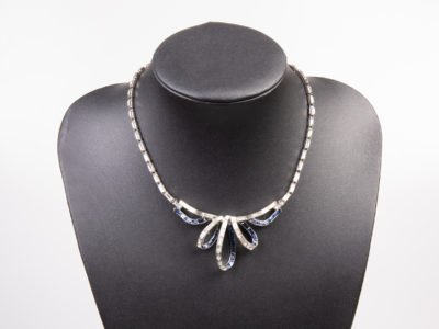 Vintage Trifari collar necklace. Glamorous collar necklace encrusted with clear and blue rhinestones with a ribbon like effect to the front. Signed Trifari to the clasp and marked patent pending. Necklace front measures 35mm at widest point in the middle of ribbon-like effect. Not adjustable. Main photo of necklace on a dark display stand