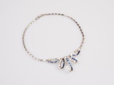 Vintage Trifari collar necklace. Glamorous collar necklace encrusted with clear and blue rhinestones with a ribbon like effect to the front. Signed Trifari to the clasp and marked patent pending. Necklace front measures 35mm at widest point in the middle of ribbon-like effect. Not adjustable. Photo of necklace on a flat surface