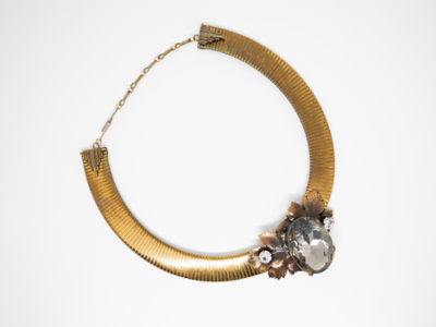 Vintage designer necklace by Ermani Bulatti. Striking design mix of Art Deco and Art Nouveau. Gilt metal choker style necklace with a bronzed leaf to the front set with a large acrylic smoky stone to the centre with Swarovski crystal to either side. Necklace is adjustable from 400mm to 485mm long. Photo of whole necklace on a flat surface with front end of necklace to the bottom right of photo