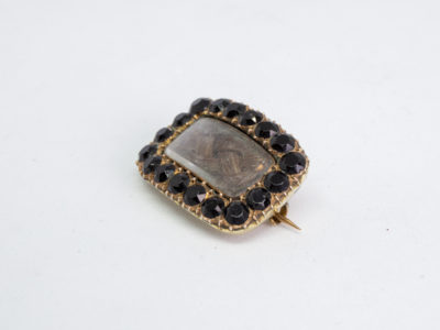 Georgian 9 karat gold mourning brooch. Small rectangular brooch with finely pleated piece of hair to the centre and framed with round cut jet stones. Beautifully inscribed in italics to the back and dated 1823. Stunning piece. Photo of brooch on a flat surface and seen with brooch front to the top left of photo
