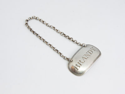 George III sterling silver decanter label. Antique sterling silver decanter label for brandy. Full hallmark and makers mark to the back (Probably George Knight, London c1812) Label measures 44mm by 25mm. Drop length approximately 70mm from centre top of chain to top edge of label. Main photo of decanter label laid flat on a surface with chain stretched out to top left and label in bottom right of photo