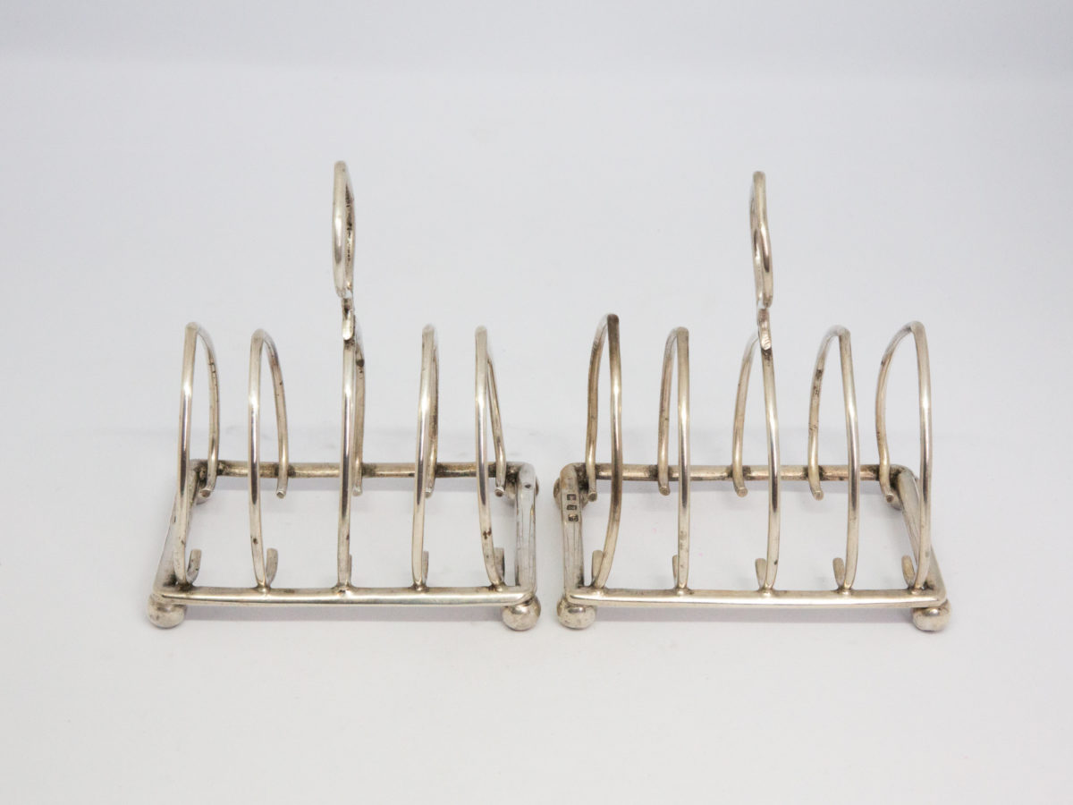 Pair of antique sterling silver toast racks. Small but sweet pair of toast racks. c1899 Birmingham assay and made by William Hutton. Each toast rack measures 72mm long, 47mm wide and 85mm tall at central point. Photo of racks side by side length ways showing some bending to a couple of racks