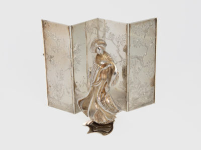 Asprey's Japanese woman and screen. Vintage Asprey's solid sterling silver figure of a Japanese woman (Geisha?) performing a dance in front of a 4 fold sterling silver screen. Hallmarked to the base of the figure and to back of each screen fold for Asprey's of London c1991. A fan is missing from figures right hand. A stunning piece of quality collectable sterling silver. Figure measures approximately 85mm tall, 45mm at widest and 40mm at deepest and weighs 253gms. Screen measures 130mm fully extended by 90mm tall and weighs 113gms. Main photo of woman posed in front of screen and seen from a near eye level angle.