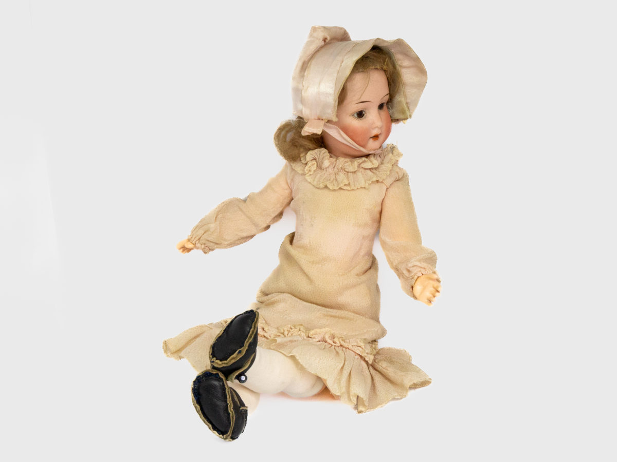 Antique Armand Marseille doll number 7. Petite bisque head doll in pale peach colour attire with incredibly realistic hand-painted features. Some wear to the clothing but otherwise in fabulous condition for a doll c1915. Measures approximately 335mm tall, 75mm wide at the hips and 55mm deep. Photo of seated doll posed with legs crossed and head turned to the right of photo.