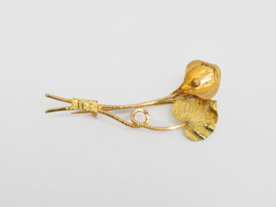 20 karat gold peace lily brooch. Modern brooch in 20 karat gold of a peace lily flower and leaf. Hallmarked XXct (for 20carat) to the base of one stem. Brooch measures approximately 48mm long and weighs 3.5gms. Box included. Main photo of brooch laid on a flat surface with flower and leaf to the right and stems to the left of photo.