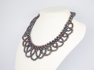 Modern black pearl necklace in a collar form. Intricately designed necklace with multiple iridescent black pearls and finished with a sterling silver clasp and slightly adjustable chain. Box included. Adjustable from approximately 400mm to 455mm. Necklace weight 57.6 grams. Photo of necklace displayed on a stand and seen at a slight angle with necklace front facing left.