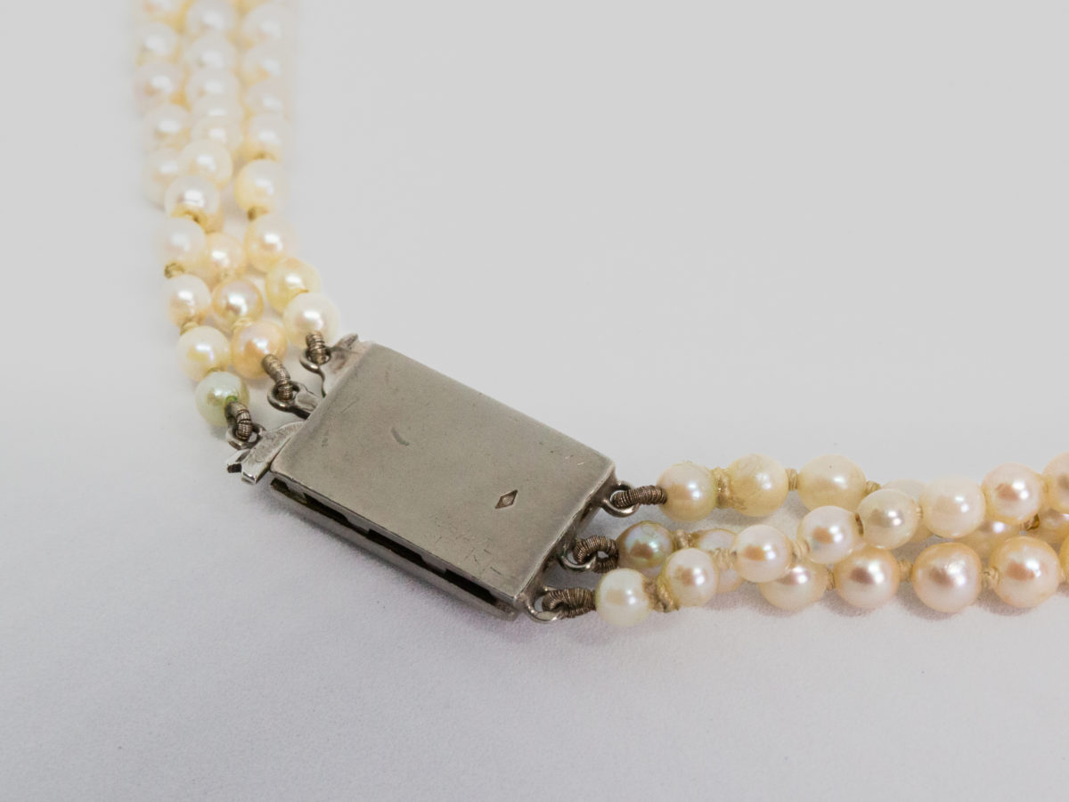 Art Deco graduated pearl necklace. Stunning necklace with 3 strands of graduated pearls and a paste stone encrusted clasp. Unidentifiable hallmark to back of clasp. Made in France. Shell shaped box included but not original. Shortest strand measures approximately 420mm and longest 450mm. Necklace weight 47gms. Close up photo of the back of clasp with hallmark visible.