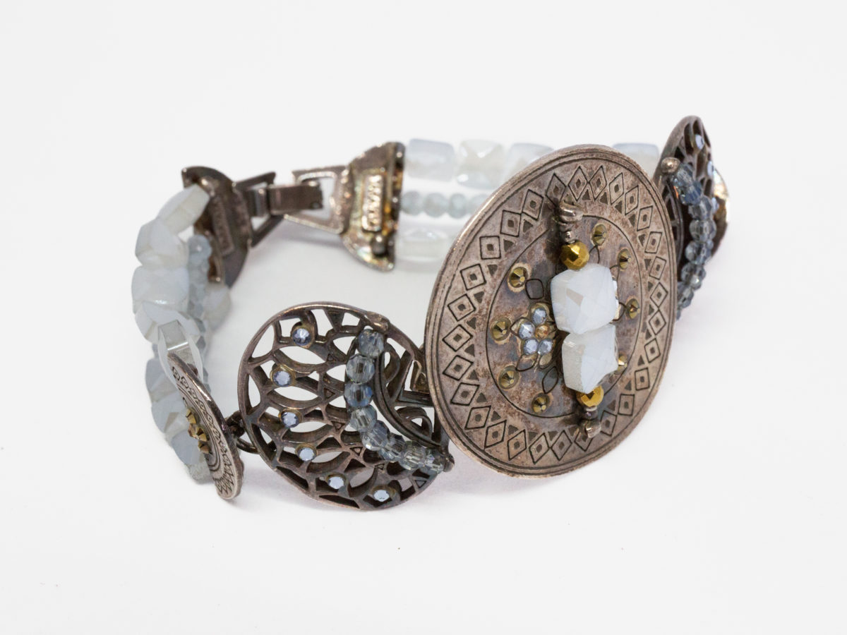 Modern Swarovski bracelet by Taratata. Very pretty bracelet evocative of ancient civilisations. Metal base set with smoky blue and gold Swarovski crystals. Made in France. Central disk measures approximately 37mm in diameter. Photo of the bracelet on a flat surface with bracelet front facing the bottom right corner of picture