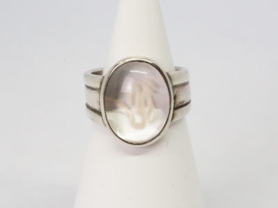 Modern vintage ring in sterling silver with Om crystal. An unusual modern vintage sterling silver ring set to the centre with smooth oval quartz crystal with the Om symbol carved into it. Crystal area measures 18mm by 10mm. Ring size P / 7.5 Main photo of ring displayed on a cone shaped stand and seen with ring front facing forward & OM sign visible.