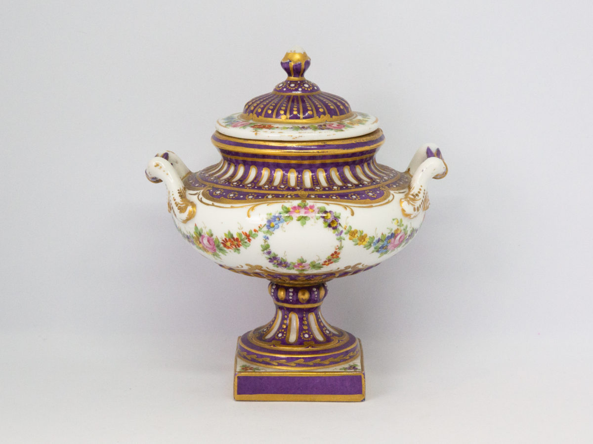 Antique Sèvres 2 handled urn with lid. Beautifully handmade and hand-painted Sèvres urn with 2 handles and lid in royal purple and gilt with floral design throughout. Some gilt wear mostly on the rim of the lid otherwise in excellent condition. Late 19th century. Base measures 55mm square, width at widest across handles 130mm, opening at top 72mm in diameter. Main photo of urn with lid in place and seen from an eye level angle with handles to left and right.