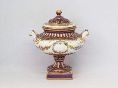 Antique Sèvres 2 handled urn with lid. Beautifully handmade and hand-painted Sèvres urn with 2 handles and lid in royal purple and gilt with floral design throughout. Some gilt wear mostly on the rim of the lid otherwise in excellent condition. Late 19th century. Base measures 55mm square, width at widest across handles 130mm, opening at top 72mm in diameter. Main photo of urn with lid in place and seen from an eye level angle with handles to left and right.