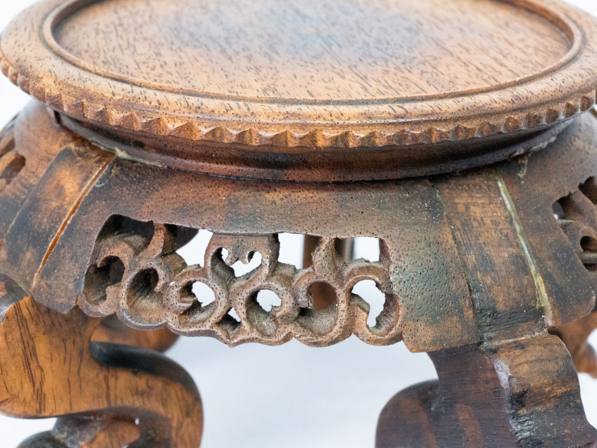 Vintage carved Chinese wooden stand. A nice sized Chinese stand in natural wood with lovely carved detail to the skirt under the stand and to the legs. Some repair work has been carried out as shown on photos. Outer diameter of top area measures 126mm and inner diameter measures 103mm. Widest area at top of legs measures 165mm. Close up photo of one edge of stand where glue used in repair is visible.