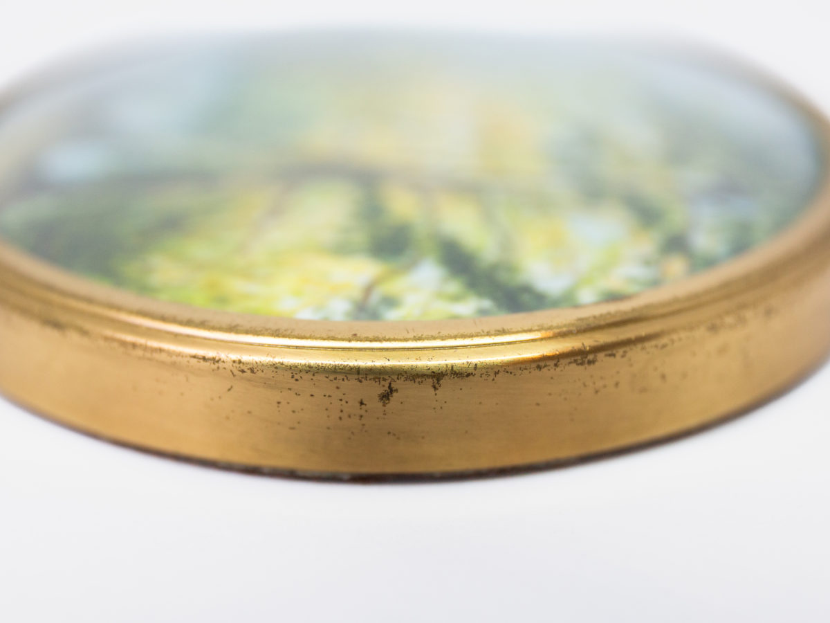 Hand-painted miniature with brass frame. Lovely hand-painted miniature of a man fishing by the river under the trees and a second person asleep. Wonderful detail to this piece of art. Measures 75mm in diameter. Drop length from top of bail measures 92mm. Close up photo of another area of the frames edge.