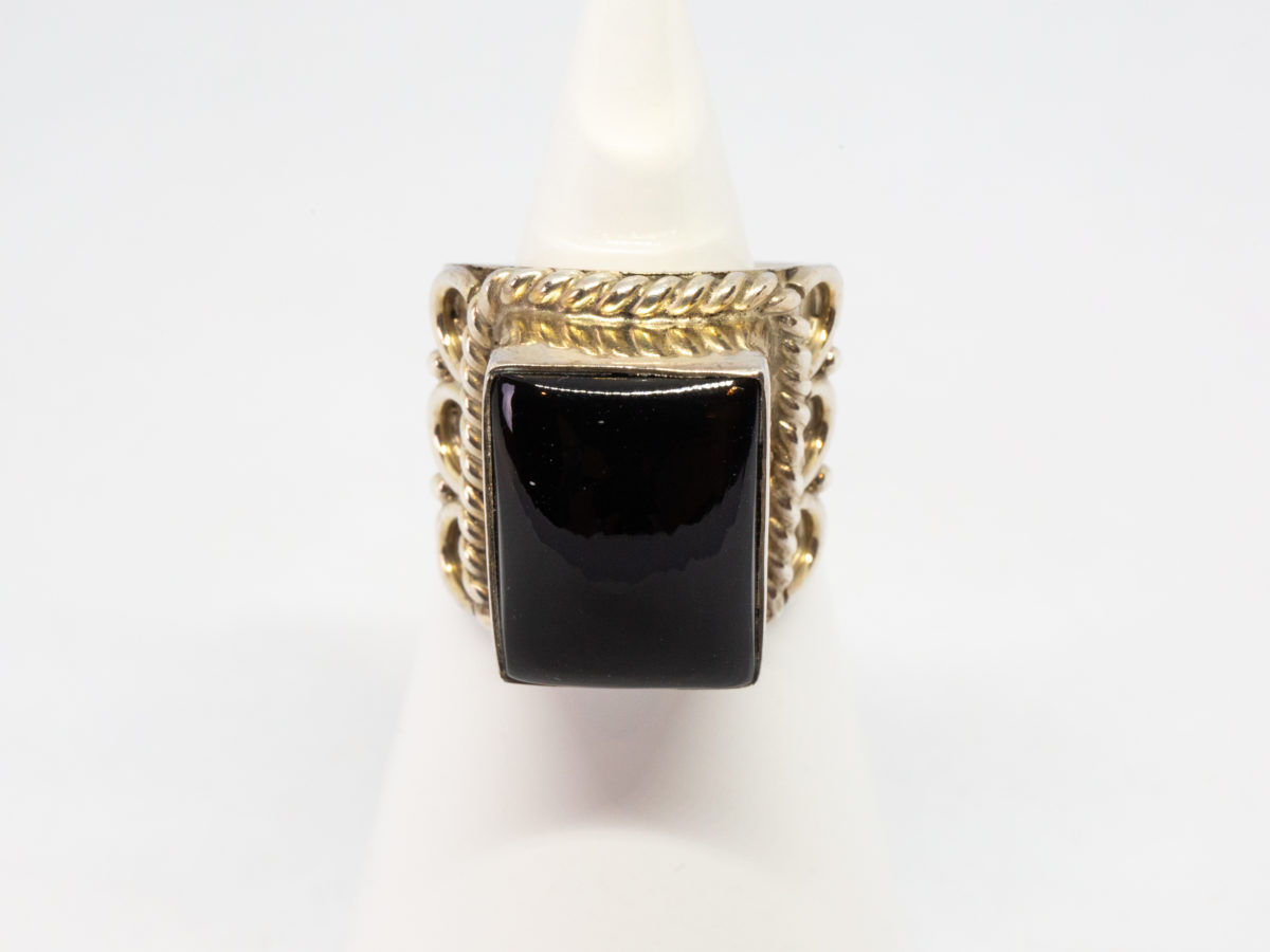 Vintage sterling silver and black onyx ring. A nice chunky sterling silver ring set with a large rectangular black onyx. Silver twist work frames the stone area. Hallmarked 925 for sterling silver. Stone measures 16mm by 12mm.  Ring size N.5-O / 7. Main photo of ring displayed on a cone shaped stand with ring front facing camera.