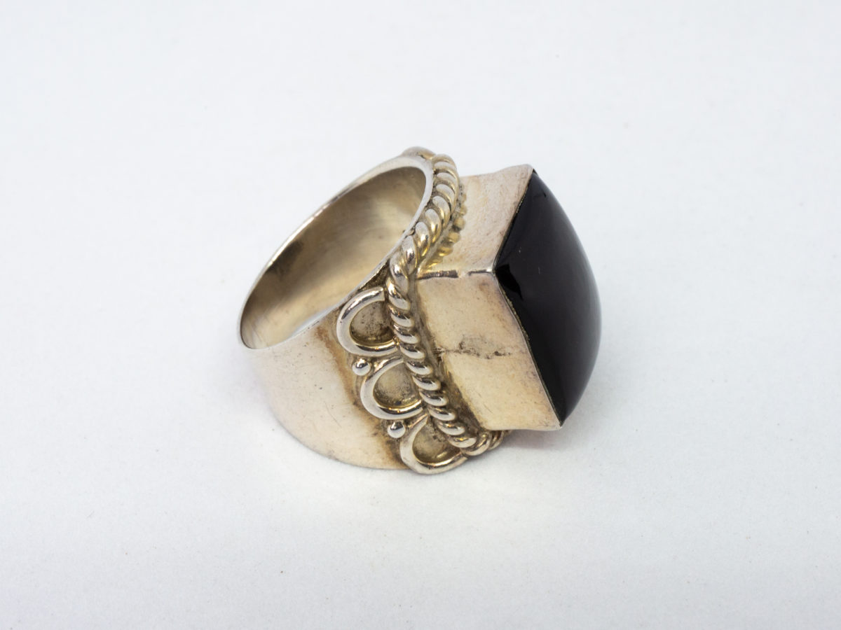 Vintage sterling silver and black onyx ring. A nice chunky sterling silver ring set with a large rectangular black onyx. Silver twist work frames the stone area. Hallmarked 925 for sterling silver. Stone measures 16mm by 12mm.  Ring size N.5-O / 7. Photo of ring on a flat surface and seen with ring front facing right of photo.