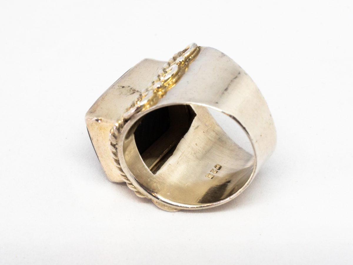 Vintage sterling silver and black onyx ring. A nice chunky sterling silver ring set with a large rectangular black onyx. Silver twist work frames the stone area. Hallmarked 925 for sterling silver. Stone measures 16mm by 12mm.  Ring size N.5-O / 7. Photo of ring laid on its side showing the thickness of the band with hallmark just visible.