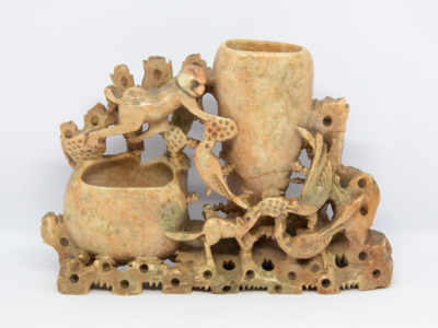 Vintage Oriental soapstone brush pot. Wonderful brush pot with a scene of wildlife gorging on lotus roots and seeds. 2 pots for brushes which are both engraved with a foliage design. Taller pot has crack across the base and both pots have sustained chips. Slight wobble from uneven base. Measures approximately 195mm at base, 35mm at widest and 132mm at tallest. Main photo showing decorative side of pot from a near eye level angle with larger of the brush pots to the right.