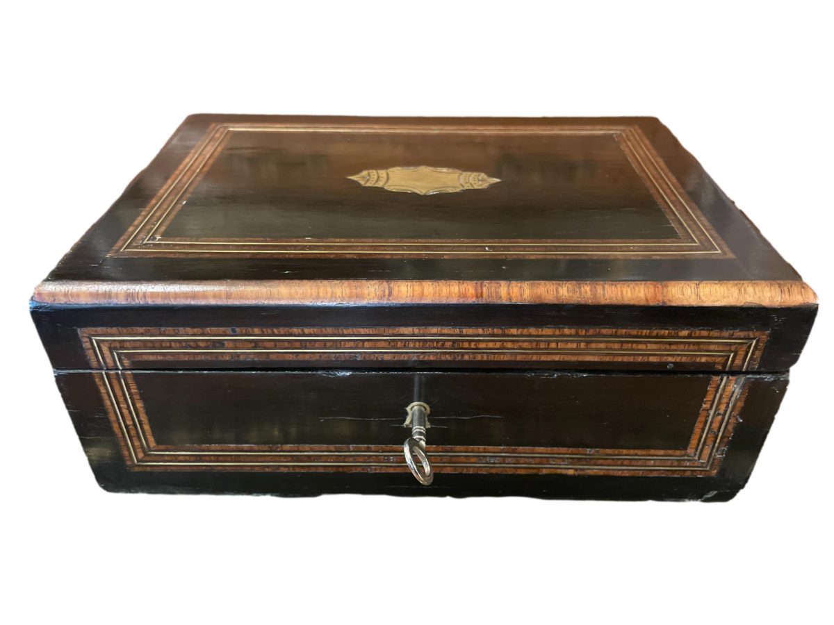 Napoleon Palais Royale sewing box with key and part original contents. Ebonised wood exterior with tulip wood veneer, brass inlay and cartouche. The inside is  lined with padded pale blue silk to the lid and base with removable tray housing the sewing tools. Napoleon III 1850-1899. Photo of box with lid closed and seen from the front with key in place.