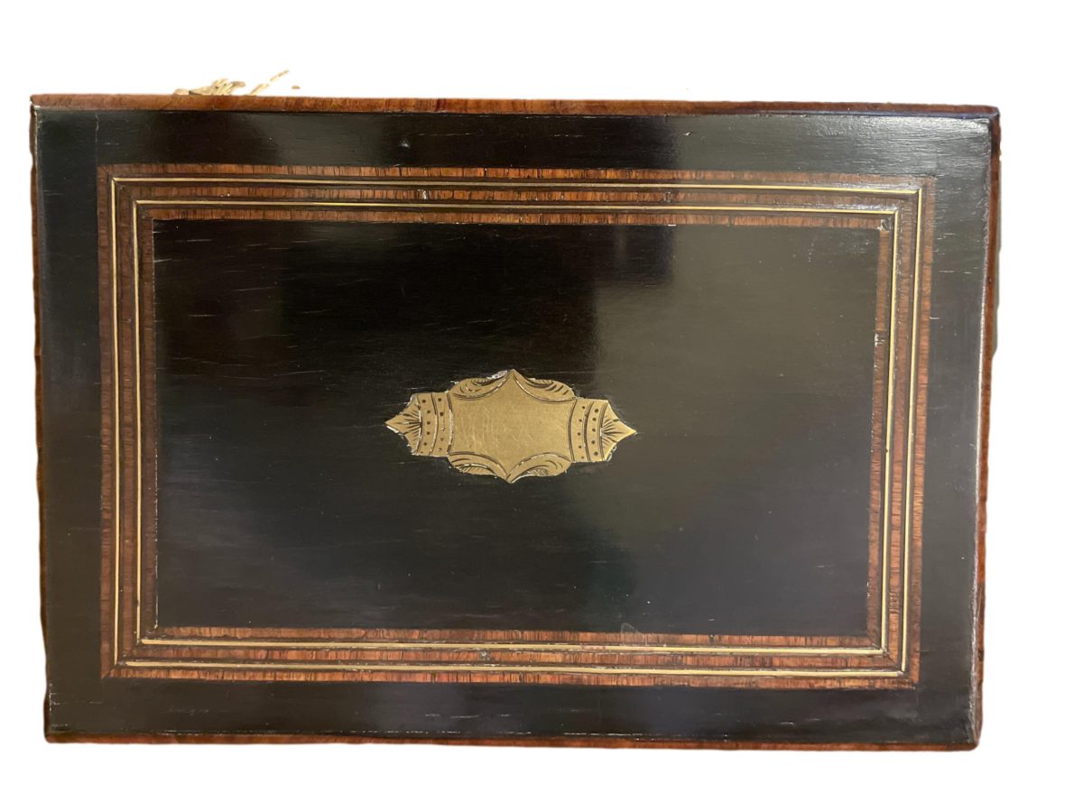 Napoleon Palais Royale sewing box with key and part original contents. Ebonised wood exterior with tulip wood veneer, brass inlay and cartouche. The inside is  lined with padded pale blue silk to the lid and base with removable tray housing the sewing tools. Napoleon III 1850-1899. Photo of top of box showing the brass cartouche to the centre.