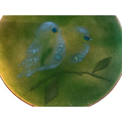 Small mid century enamel on copper plate by Judith Wedemeier USA c1960s. Beautiful green enamel dish decorated with 2 pale blue birds sat on a branch with raised bubble accents for the birds eyes and breasts. Signed Wedemeier USA to the base. There are 3 shallow indents to the base possibly from manufacturing process. Measures 125mm in diameter.Close up of the 2 little blue birds and the branch they are sat on.