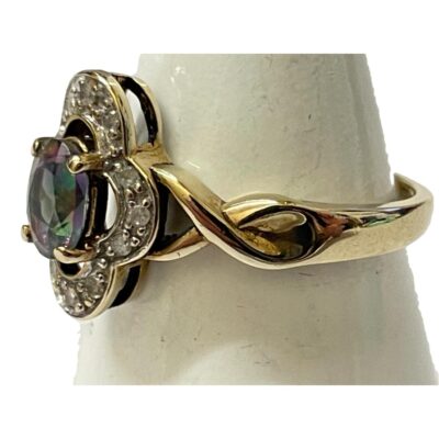 A 9ct gold Gypsy ring size M with a colourful Mystic stone and diamond setting. Close up of the ring on a cone shaped stand with the ring front facing left. The twist split band shoulder is clearly visible.