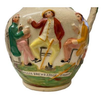 The vintage jug with three friends enjoying a beer features an amusing scene amongst the hops and vines. Beautifully hand- painted and extremely decorative it will brighten any room. Some signs of crazing. COLLECT FROM STORE ONLY. Close up photo of the 3 friends drinking with words 'Willie brewd apeck omaut' below the figures drinking.