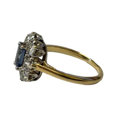 Vintage 18 karat gold ring set with an emerald cut cornflower blue sapphire to centre and a frame of 8 brilliant classic round cut diamonds. Gems are set on 18 karat white gold with an 18 karat yellow gold band. Ring size L.5 / 6. Box included (may not be box shown). Photo of ring shown from a side angle with ring front facing left.