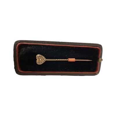 Antique stick pin with a small 9 karat gold heart with seed pearls. Hallmarked 9ct to the back of heart. The pin is in gilt metal with signs of gilt wear and is slightly bent at the top. Comes in original case. Pin measures 56mm long. Heart is 8mm at widest. Box has wear on the outside and to interior silk. Photo of pin displayed inside the case.