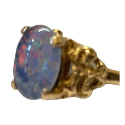 Fine quality 9 karat gold ring set with a black opal cabochon. The doublet triplet black opal emits flashes of pink, yellow & green and measures approximately 18mm by 9mm. Ring size O / 7.25. Photo of ring in a little more close up with the ring front facing left. The light is catching the stone which is now pale blue lilac in colour with pinks reds blues and greens dancing within.