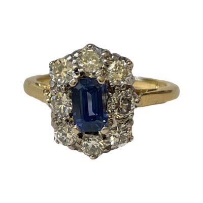 Vintage 18 karat gold ring set with an emerald cut cornflower blue sapphire to centre and a frame of 8 brilliant classic round cut diamonds. Gems are set on 18 karat white gold with an 18 karat yellow gold band. Ring size L.5 / 6. Box included (may not be box shown). Main photo of ring shown with ring front forward facing.