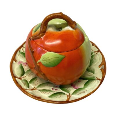 An almost antique Carlton Ware apple shaped preserve pot. Colourful hand-painted preserve pot in the form of an apple nestled on top of a bed of foliage. There are signs of crazing and staining expected with item age. The attached saucer measures 140mm in diameter. The whole ensemble is 95mm in height with lid in place. Main photo of preserve pot seen from a raised eye level angle with red side of apple with leaf in the foreground.