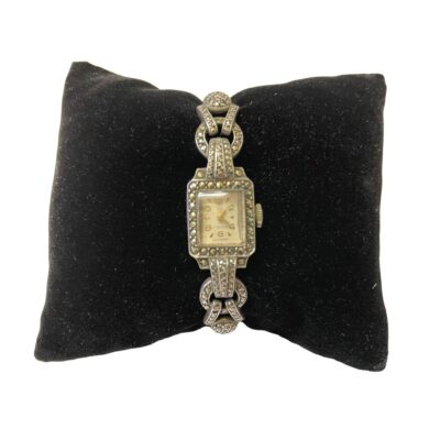 Art Deco cocktail watch in 835 silver with marcasite to the front. Watch face is marked 17 rubis EB Suisse. Worn inscription on the back which is difficult to read - last line reads Brooklyn PA. 835 silver hallmark to the back. Nice watch that keeps good time with clasp in good working order. Watch face is tiny & measures approximately 10 by 8mm. Main photo of watch displayed on a black velvet cushion and showing the watch face.