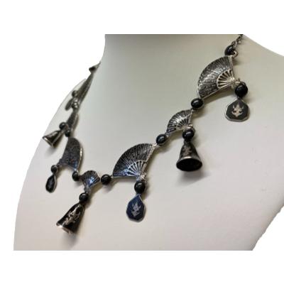Vintage Siam sterling silver Niello enamel fan necklace. Statement necklace in sterling silver with black enamelling . Main body of necklace has fans of 2 sizes with bells and discs decorated with traditional Siamese dancers. Hallmarked Siam Sterling to the back. Drop length at front (bell & small fan) is 32mm. Photo of necklace displayed on a stand and shown from a slight side angle.