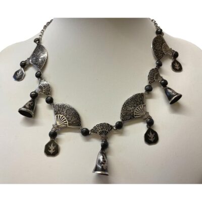 Vintage Siam sterling silver Niello enamel fan necklace. Statement necklace in sterling silver with black enamelling . Main body of necklace has fans of 2 sizes with bells and discs decorated with traditional Siamese dancers. Hallmarked Siam Sterling to the back. Drop length at front (bell & small fan) is 32mm. Main photo of necklace displayed on a stand and shown from the front.