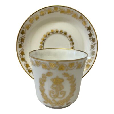 Antique Sêvres cup and saucer in white with monogrammed LP between a garland of vine leaves and a frieze of ivy leaves. Dated to c1846 in the reign of King Louis Philippe. Saucer measures 85mm in diameter at base & 125mm at top. Cup measures 35mm in diameter at base, 68mm in diameter at top, 85mm at widest to handle and 62mm tall. Main photo with cup placed in front of the saucer which is displayed upright on a stand. The decorated side of cup (opposite end to handle) is shown.