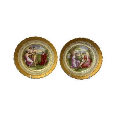 Pair of highly decorative side plates in neo classical Royal Vienna style. Both plates have heavy gilt edging and images of figures in brightly coloured neo classical dress. Each plate is signed Angelica Kauffman to the bottom of the images and marked with a beehive stamp and initials B&L to the back. Each measures approximately 155mm in diameter. Some signs of paint wear to both images. Main photo of both plates displayed upright and side by side.