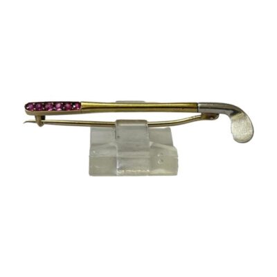 Art Deco golf putter brooch. Fabulous brooch in the form of a putter with platinum head, gold bar and handle set with 6 small round cut rubies. Tested - no visible markings . Weight 2.5gms. Main photo of golf club displayed on a stand with the ruby handle end to the left and platinum putter end on the right. The head of the putter is facing downwards.