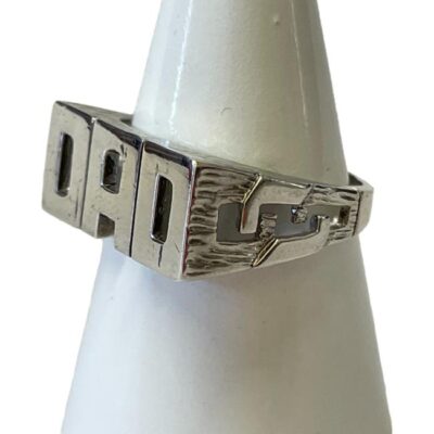 Sterling silver DAD ring. Modern ring in sterling silver with DAD spelt out to the front. Interesting chain like work to the shoulders. Hallmarked 925 for sterling silver. Ring size W.5 / 11.25 Ring weight 7.2gms. Photo of ring on a cone shaped stand and shown with ring front facing towards the left. The flat curb chain like detail of the shoulder is visible.