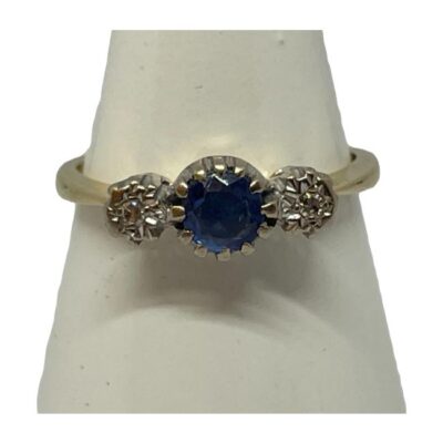 18 karat gold sapphire and diamond ring. Vintage ring in 18 karat gold with a round cut sapphire to the centre with small round cut diamonds to either side. The gem stone mount is in 18 karat white gold which accentuates the stones. Hallmarked 18ct. Ring size N.25 / 6.75. Ring weight 3.2gms Main photo of ring on a cone shaped stand with ring front facing forward.