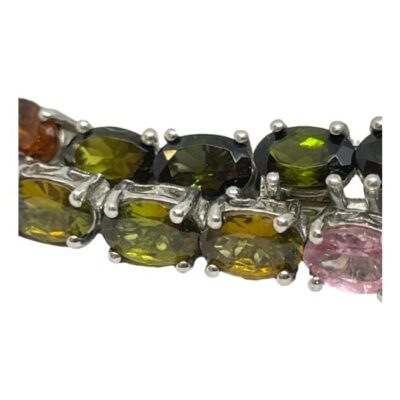 Sterling silver bracelet with multi-coloured tourmaline. Modern silver tennis bracelet set with oval cut tourmaline in a variety of colours with a rainbow like look. Hallmarked 925 for sterling silver, the clasp pin end is marked metal. Close up photo of some of the different colours of tourmaline stones from pale pink to orange to green.