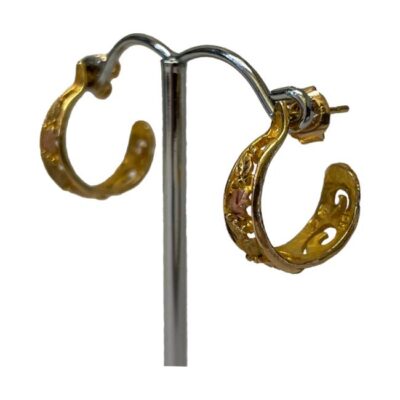 Open hoop earrings in 3 coloured gold. Black Hills 10 karat 3 colour gold open hoop earrings with grape and vine decoration. Hallmarked 10k to back of earrings. The butterfly fasteners are hallmarked for 14 karat gold and are not identical.. Hanging length 18mm, width graduates from 3mm to 6mm. Photo of both earrings on a contrasting silver coloured display stand and shown from a slight side angle with one earring to the foreground and in the bottom right while other is seen to the back slightly in the top left.