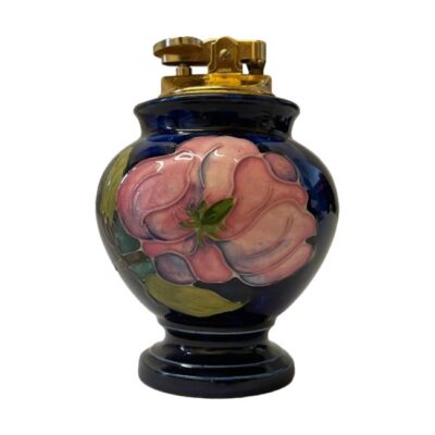Moorcroft table lighter in magnolia pattern. c1950s magnolia pattern table lighter with pink magnolias set against a dark blue background. Impressed Moorcroft stamp to the base. The lighter is in good working order. Measures 52mm at base and approximately 70mm at widest mid area. Photo of lighter seen from an eye level with the open magnolia side visible.