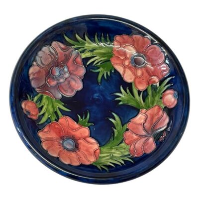 Moorcroft dish in anemone pattern. Mid sized Moorcroft dish in dark blue with light purple/red anemone flowers. Signed to the back for Walter Moorcroft and dates to between 1947-1953. Impressed stamps to the base and painted initials. Measures 110mm at base and 220mm across the top. Main photo showing the dish in full and looking straight on at the dark pink and purple anemone flowers against the famous blue background that Moorcroft is noted for.