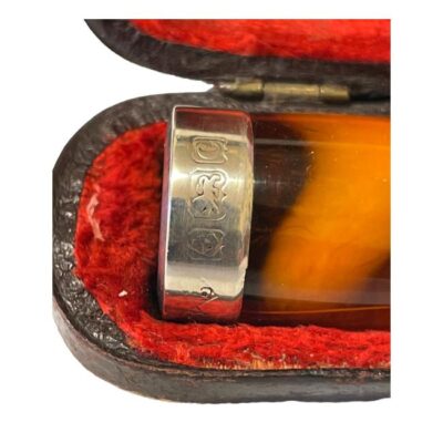 Amber cheroot holder with silver band. Antique cheroot holder with a sterling silver band to the cheroot end. Comes in original fitted case with red velvet lining. Fully hallmarked to the silver band for Birmingham assay c1902. Some wear to outer case. Cheroot holder measures 68mm long. Close up photo of the silver band at the end of the cheroot holder showing the hallmark.
