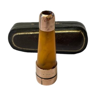 9 karat gold and amber cheroot holder. Small amber cheroot holder in original case with 9 karat rose gold bands. The 2 gold bands at outer extremes are fully hallmarked for Birmingham assay c1911. The second inner band is hallmarked for a later date and has probably been replaced. Comes complete with original fitted case. Cheroot holder measures 48mm long. Photo of cheroot holder displayed upright and in front of closed case which is laid on its side.