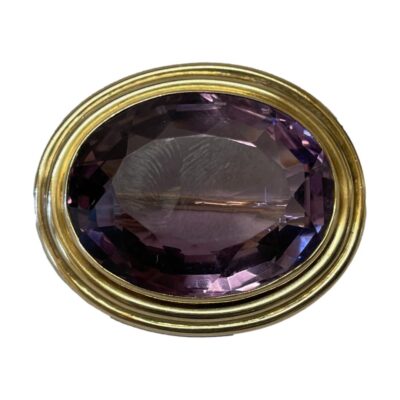 14 karat gold brooch with amethyst. Elegant 14 karat gold brooch with a large faceted amethyst to the centre. The brooch features a double security clasp with the pin shaped to lie tightly across the stone. There is also a rectangular hook for wearing as a pendant. Main photo of brooch seen looking straight on from the front.